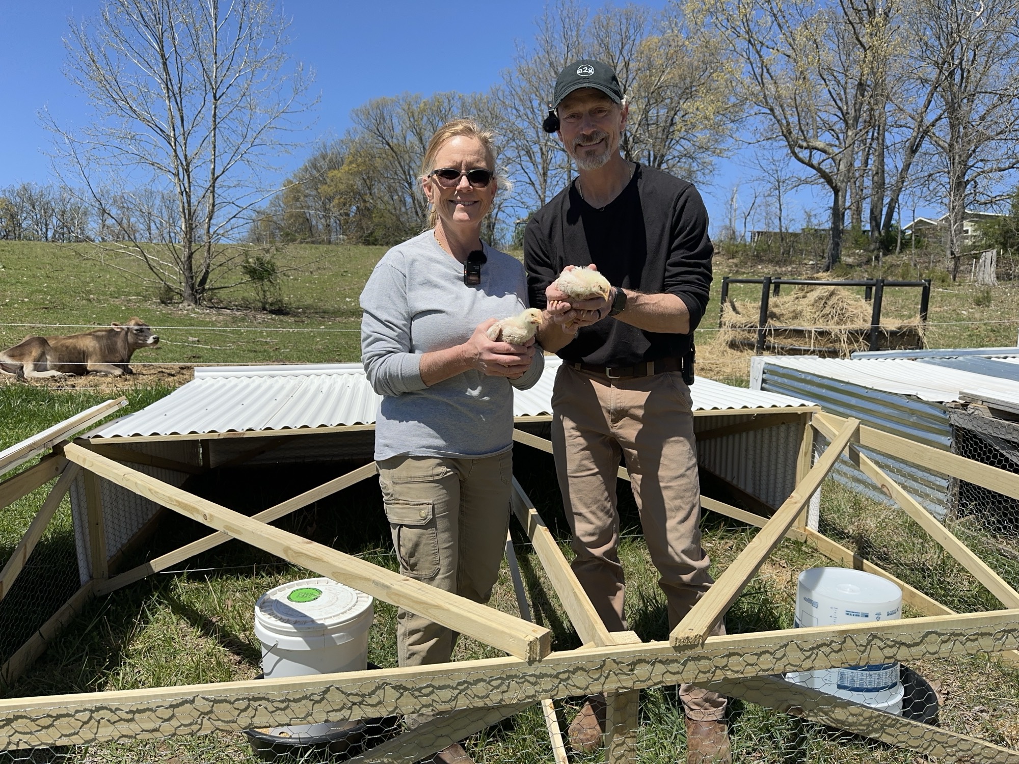 Rich and Shelley holding Cornish Cross chicks in front of Salatin-style chicken tractor in green pasture